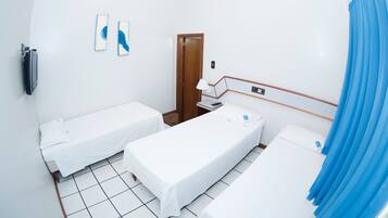 A hotel room with two single beds, a small table, a chair, a TV, and a bathroom with a shower curtain.