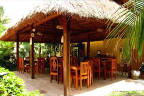An outdoor wooden structure with a thatched roof, surrounded by wooden chairs and tables, set in a lush green environment. - Hotel Maya Balam (Calakmul)
