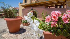 A building with a balcony and a flower bed with white and pink flowers. - Skandalis Traditional Suites (Chania)