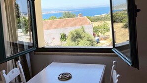 A room with a table and chairs, a window with an open shutter, and a view of the sea and buildings. - Skandalis Traditional Suites (Chania)