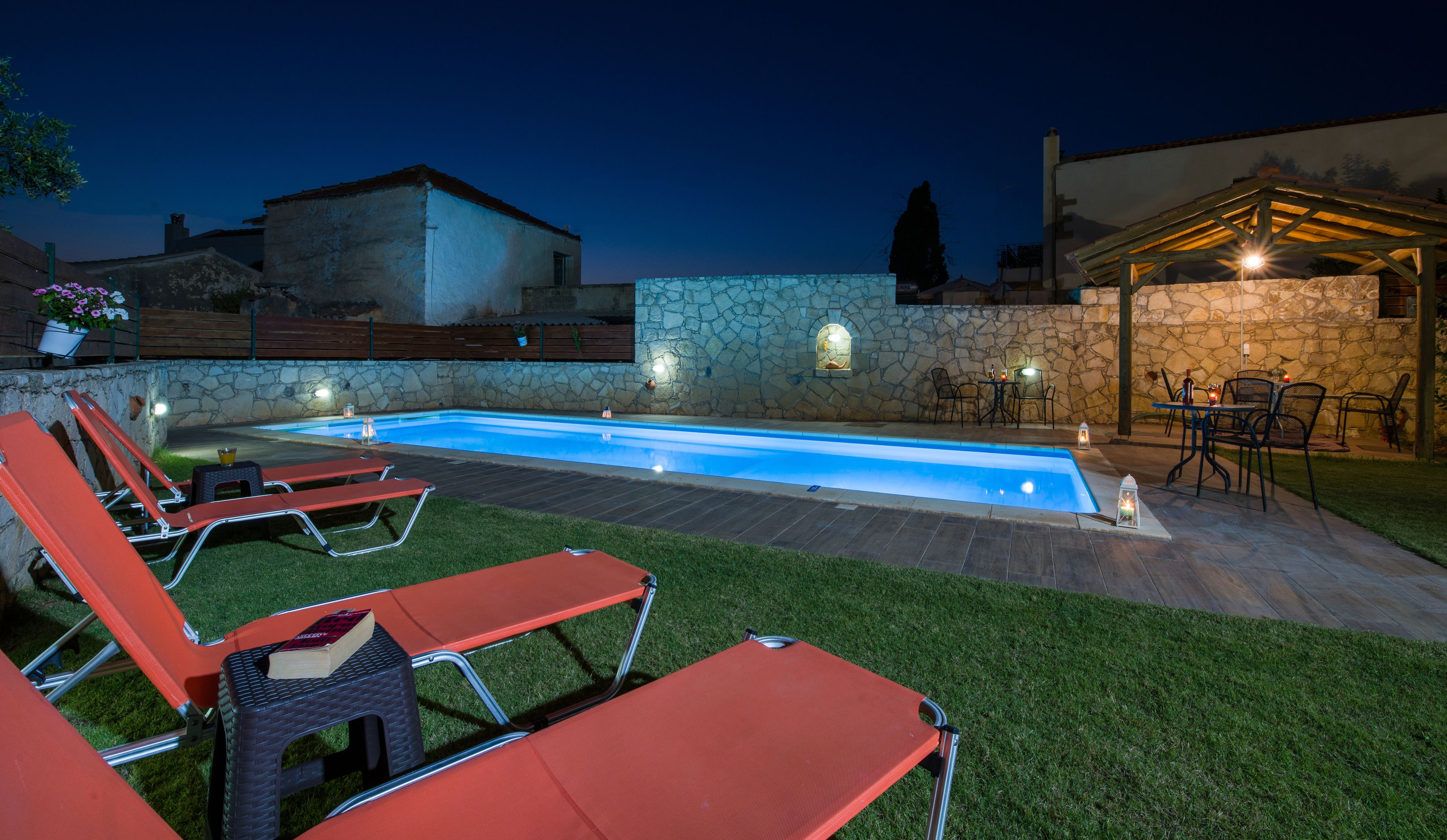 A swimming pool with a stone wall and a patio area with outdoor seating.