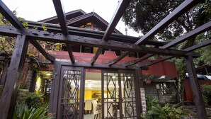 Una estructura de pérgola de madera con un ventanal de vidrio que da a un espacio interior con mesas y sillas.