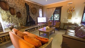 Una sala de estar acogedora con pared de piedra, chimenea, televisor, mobiliario de mimbre y sofá de cuero.