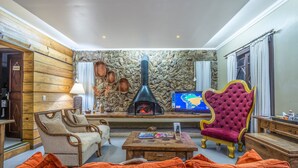Una sala de estar acogedora con pared de piedra, chimenea, televisor y asientos cómodos.