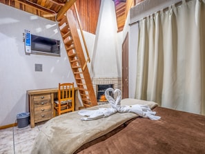 A bedroom with a wooden ladder, a fireplace, a bed with towels, and a wooden dresser. - Alameda Paradiso Hotel (Gramado)