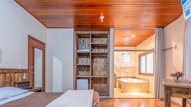 Un dormitorio con techo de madera, una cama, un armario y un baño con bañera y paredes de azulejos.