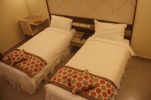 Una habitación de hotel con dos camas individuales, una mesita con una cesta de naranjas y un teléfono junto a la cama.