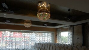A spacious hall with rows of white chairs, large windows with patterned curtains, and two large, spherical chandeliers. - Buhari Royale Boutique Hotel (Chennai)