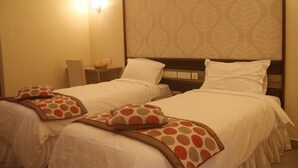 A hotel room with two beds, each with white bedding and decorative pillows. There is a bedside table with a lamp and a basket. - Buhari Royale Boutique Hotel (Chennai)