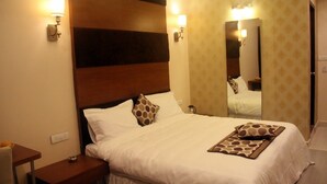 A hotel room with a large bed, two bedside tables, a nightstand, a mirror, and wall sconces. - Buhari Royale Boutique Hotel (Chennai)
