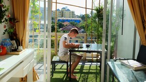 A room with a glass table, a chair, and a view of buildings through a window with curtains. - Baan Sabai Rama IV (Bangkok)