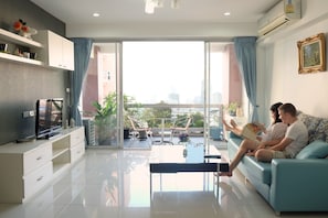 Ein modernes Wohnzimmer mit einer Couch, einem Fernseher und einem Balkon mit Pflanzen.