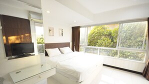 A modern bedroom with a large bed, a glass bedside table, a flat-screen TV mounted on the wall, and a large window with a view of greenery outside. - Baan Sabai Rama IV (Bangkok)