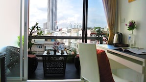 A balcony with a view of a tall building, a table with chairs, and a desk with a chair and a vase of flowers. - Baan Sabai Rama IV (Bangkok)