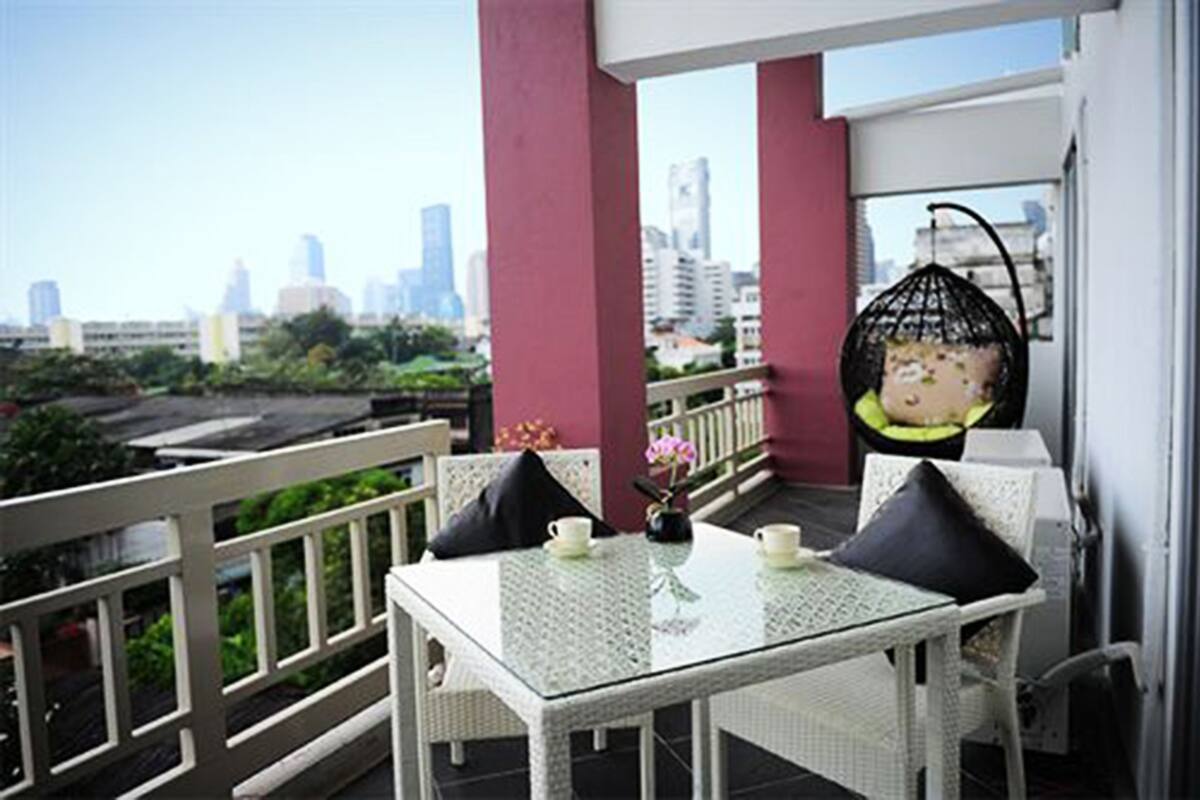 A balcony with a glass table and chairs, a hanging chair, and a view of a city skyline.