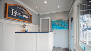 A reception area with a sign reading "Welcome to The Buccaneer Inn," a reception desk, a framed map on the wall, and a door leading to another room. - Buccaneer Inn (Nanaimo)