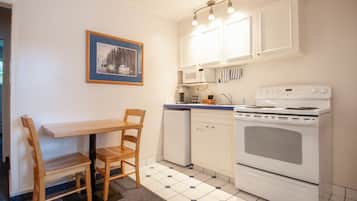Una cocina con armarios blancos, estufa, microondas y una mesa de comedor con sillas.