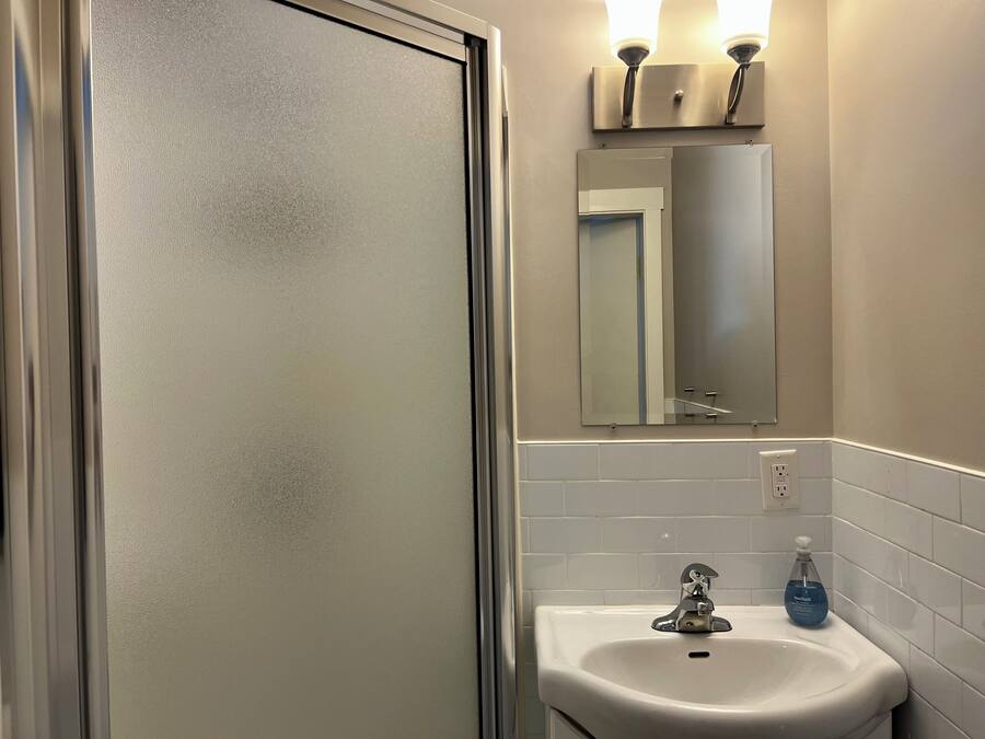 Un baño con lavamanos blanco, espejo y puerta de vidrio satinado.