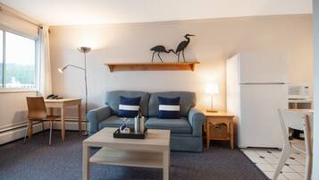 A compact living space with a sofa, a coffee table, a dining table, and a refrigerator.
