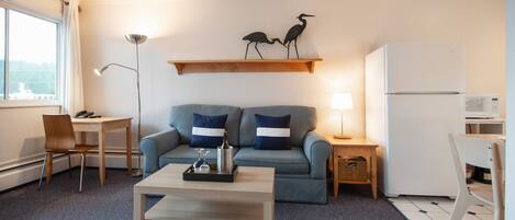 A compact living space with a sofa, a coffee table, a dining table, and a refrigerator.
