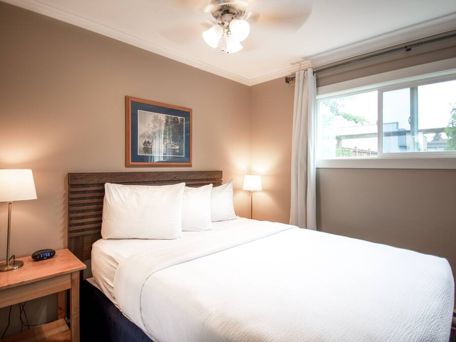 A hotel room with a large bed, two bedside lamps, a framed picture on the wall, and a window with curtains.