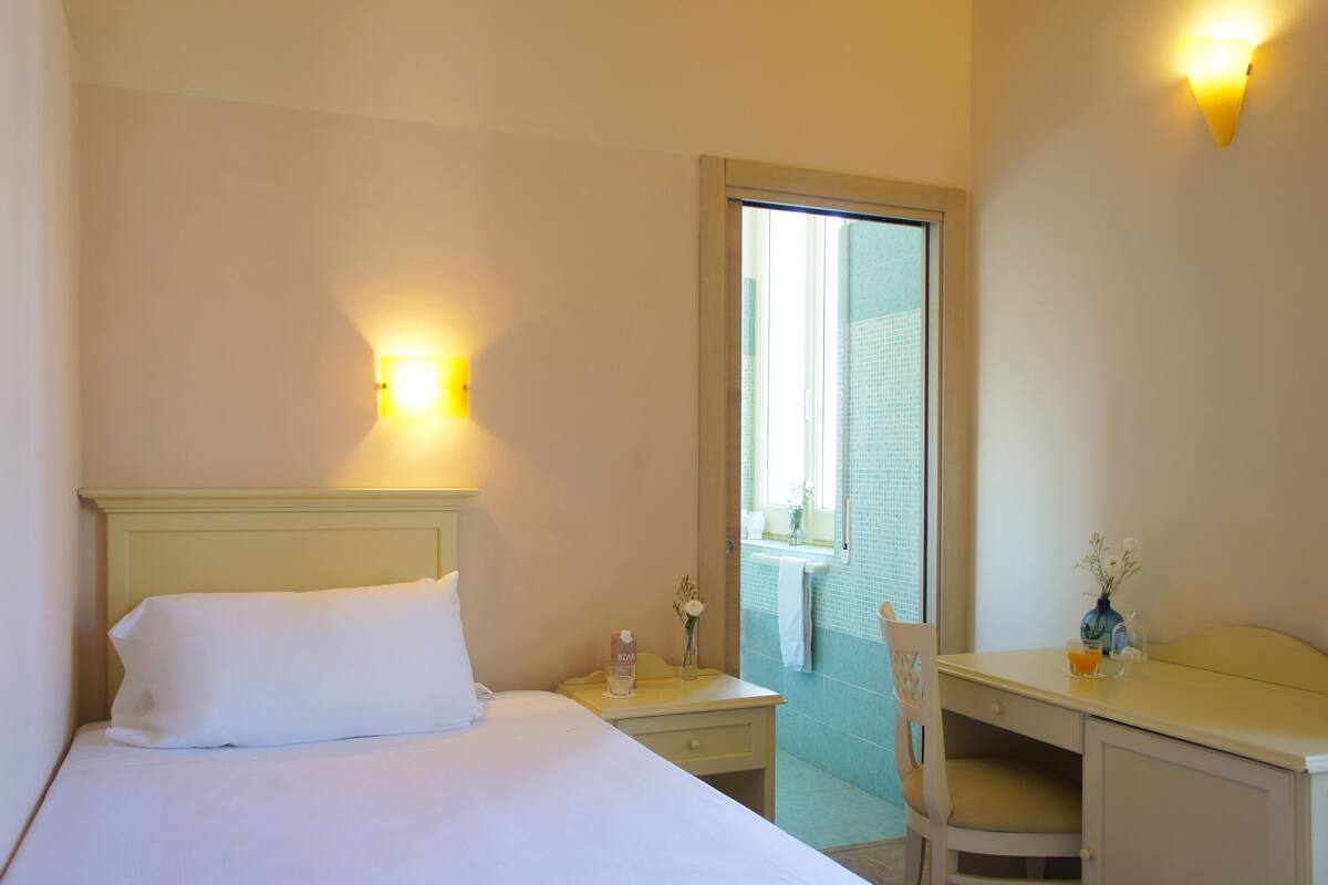 A hotel room with a bed, a desk, a chair, a nightstand, and a bathroom visible through an open door.