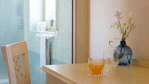 A table with a glass of orange juice, a vase with white flowers, and a blue vase with a plant. - Hotel Le Muse (Syracuse)