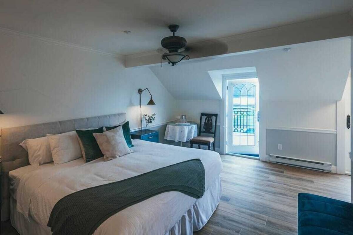 A bedroom with a large bed, a desk, a chair, a ceiling fan, and a view of the outside through a window.