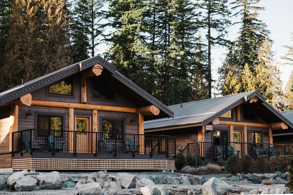 A log cabin with a porch, large windows, and a stone foundation.