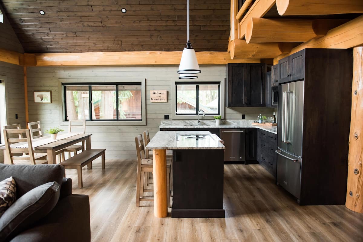 A modern kitchen with wooden cabinetry, a central island, and a dining area with a sofa and chairs.