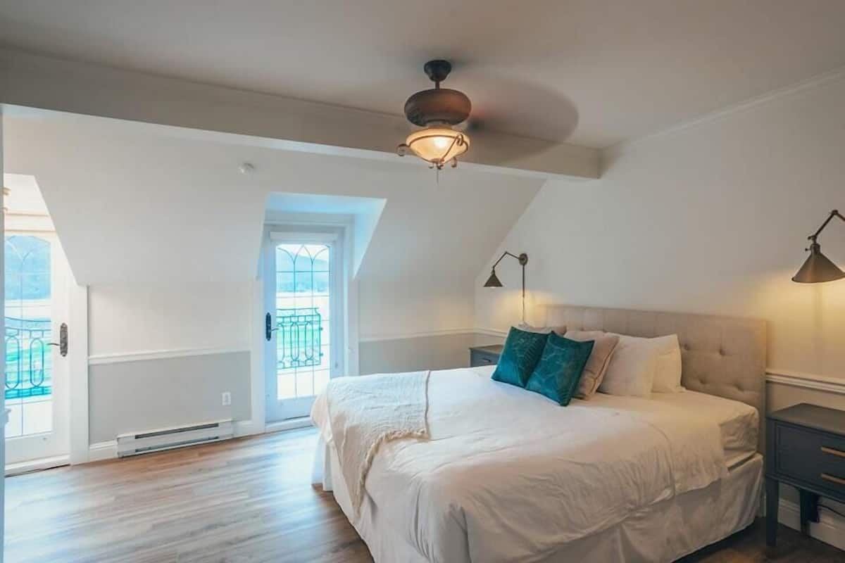 A bedroom with a large bed, a ceiling fan, a nightstand, and a window with a view of the outdoors.