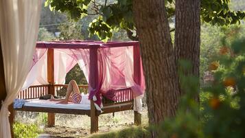 Relax under a shaded tree in a serene natural setting, surrounded by lush greenery and a clear view of the sky.
