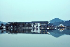 A large building with multiple floors, a reflection in the water, and a hilly landscape in the background. - Tianmushan Hotspring Hotel (Yichun)