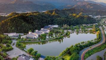 Um resort à beira de um lago, com edifícios, uma estrada sinuosa e colinas arborizadas ao redor.