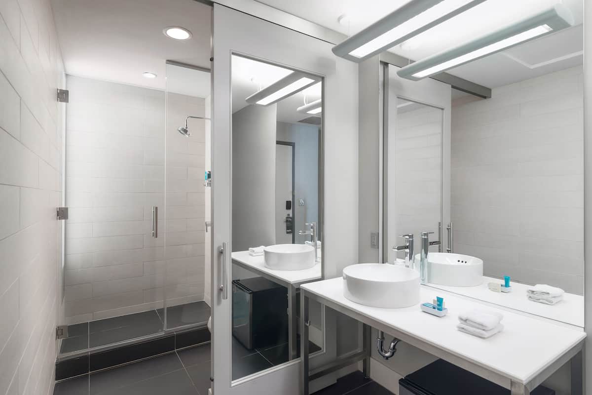 A modern bathroom with two sinks, a glass shower enclosure, and a large mirror.
