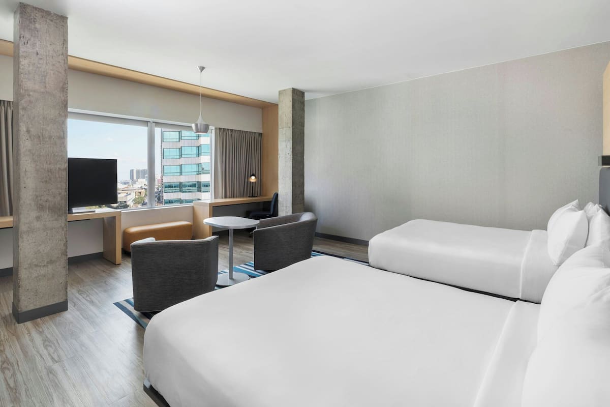 A hotel room with a large bed, a desk with a chair, a small table, and a TV.