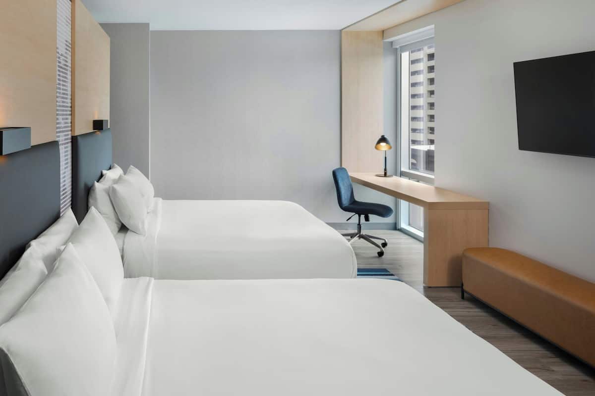 A modern hotel room with two beds, a desk, a chair, and a TV.