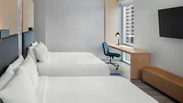 A modern hotel room with two beds, a desk, a chair, and a TV.