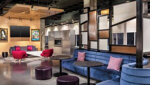 A modern lounge area with a blue sofa, red chairs, and round tables. - Aloft by Marriott Tampa Downtown (Tampa)