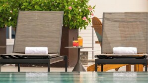 Two lounge chairs with white towels, a pool, and a potted plant with pink flowers. - Aloft by Marriott Tampa Downtown (Tampa)