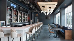 A modern bar area with a long counter, bar stools, and seating with tables and chairs. - Aloft by Marriott Tampa Downtown (Tampa)