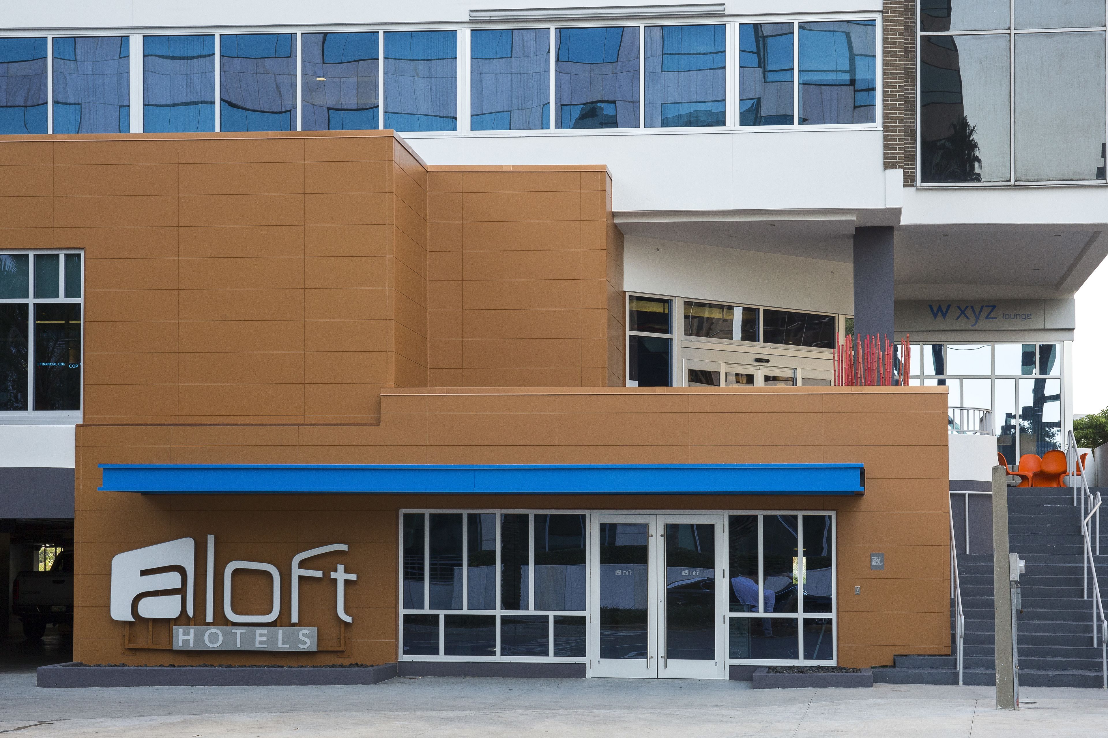 Ein modernes Hotel mit einem gut sichtbaren 'aloft hotels' Schild, großen Fenstern und einer blauen Markise.