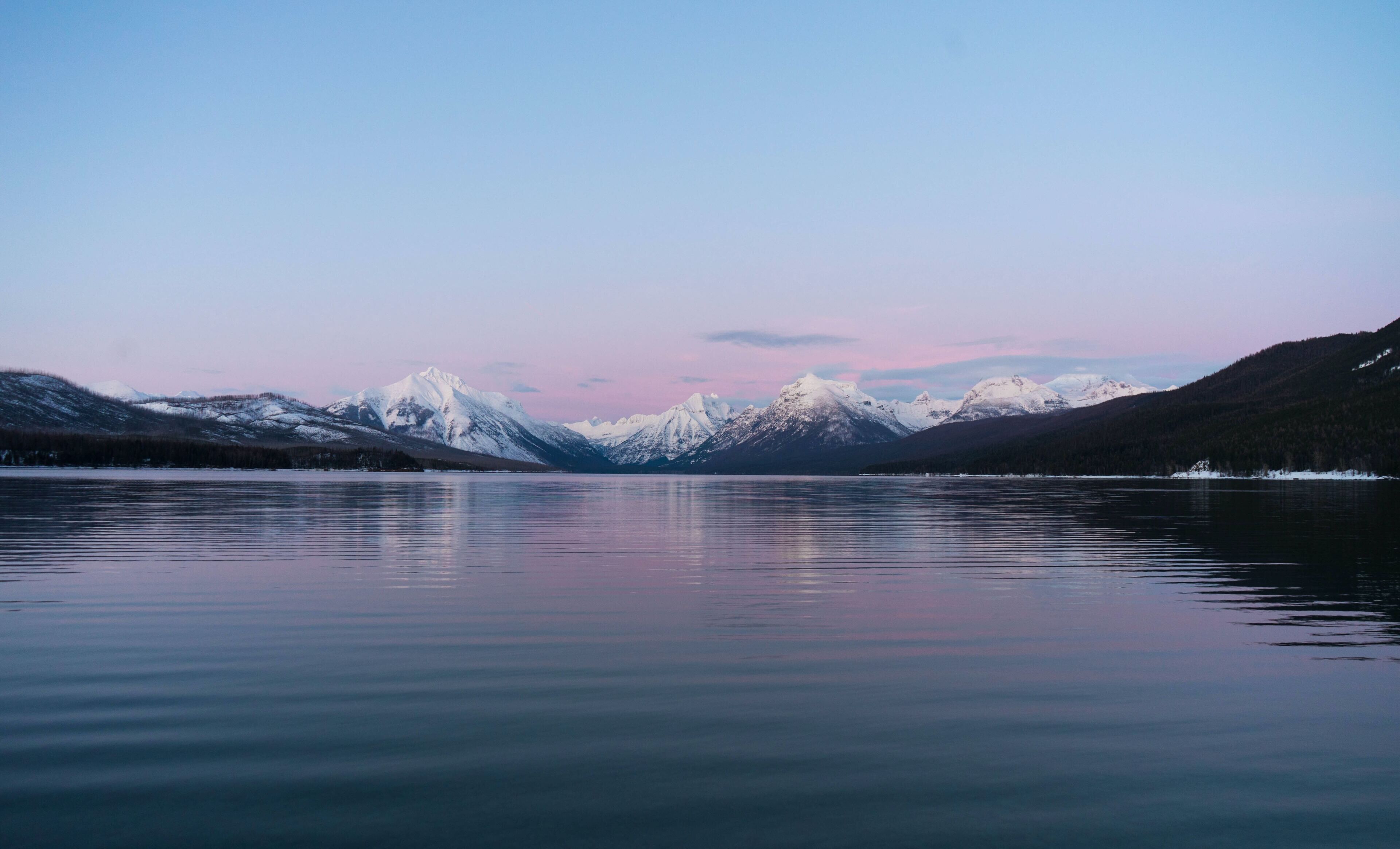 Un lago tranquilo con montañas nevadas al fondo.