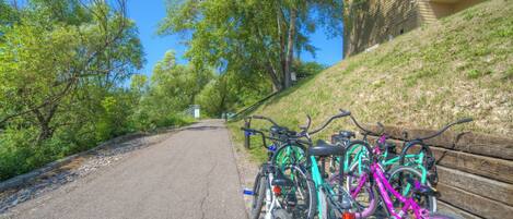 A paved path with bicycles parked on the side, surrounded by trees and a building with a balcony.