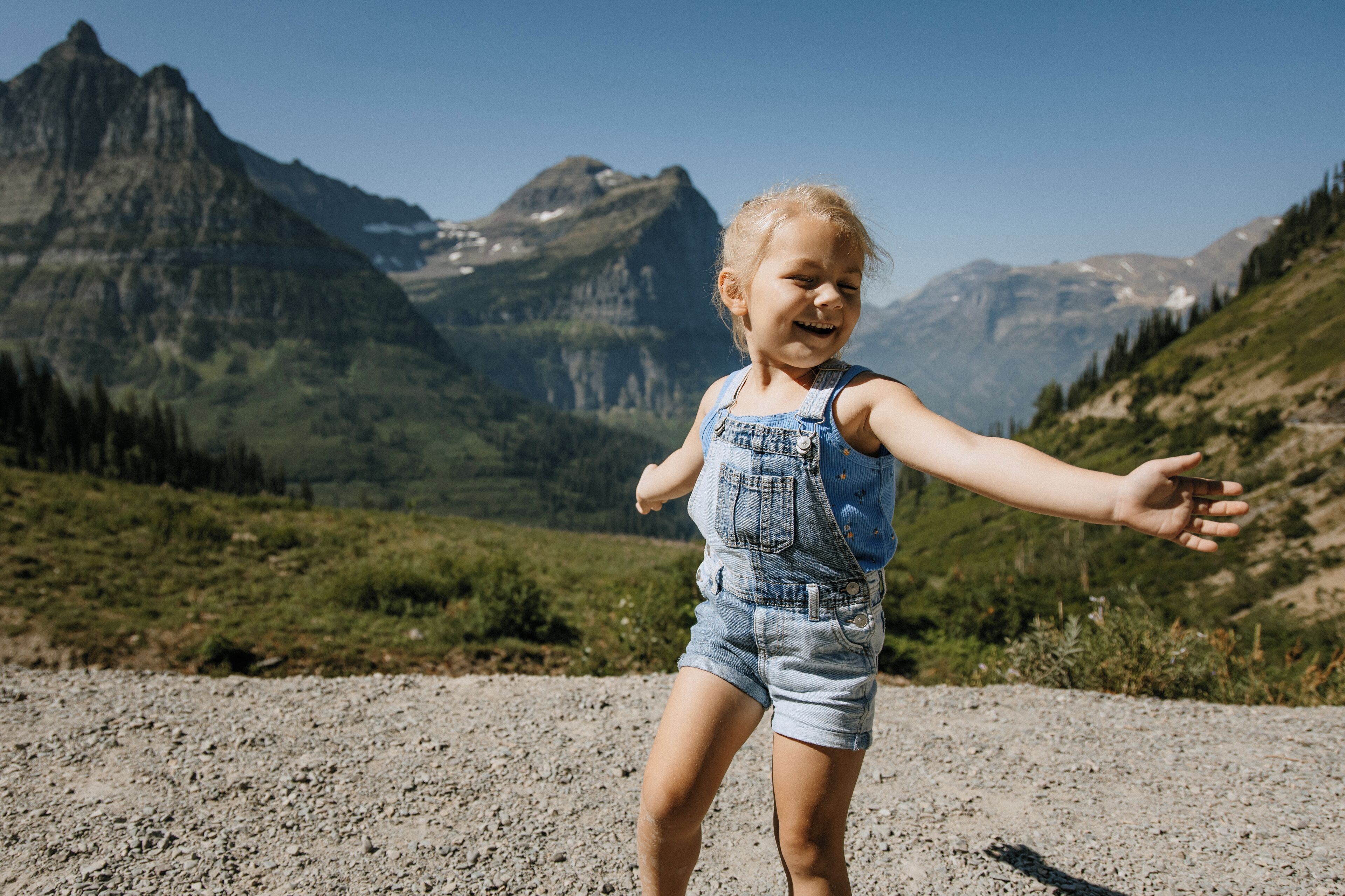 A child standing on a gravel path with a mountainous landscape in the background.