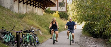 Two people riding bicycles on a paved path with bicycles parked on the side.