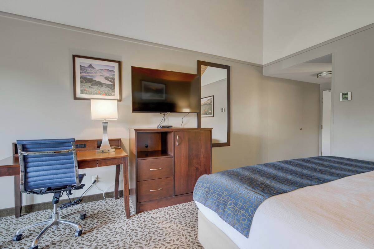 Een hotelkamer met een bed, een bureau met een stoel, een dressoir, een televisie en een ingelijst schilderij aan de muur.