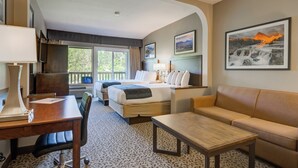 Ett hotellrum med två sängar, en soffa, ett skrivbord och en stol. Det finns fönster med utsikt över träd och en målning av ett vattenfall på väggen.