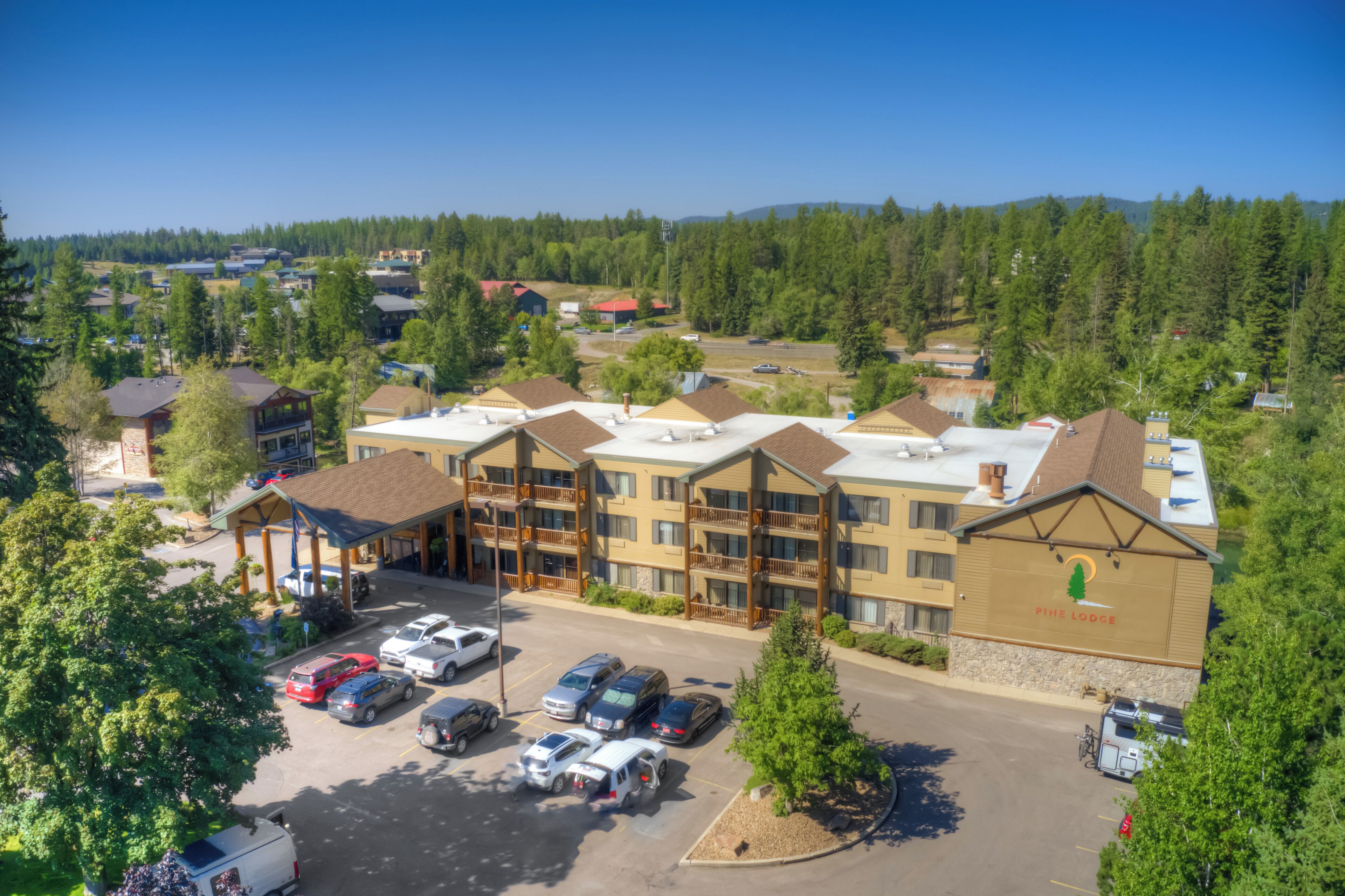 Ein mehrstöckiges Hotel mit Parkplatz, umgeben von Bäumen und einem Bergpanorama.
