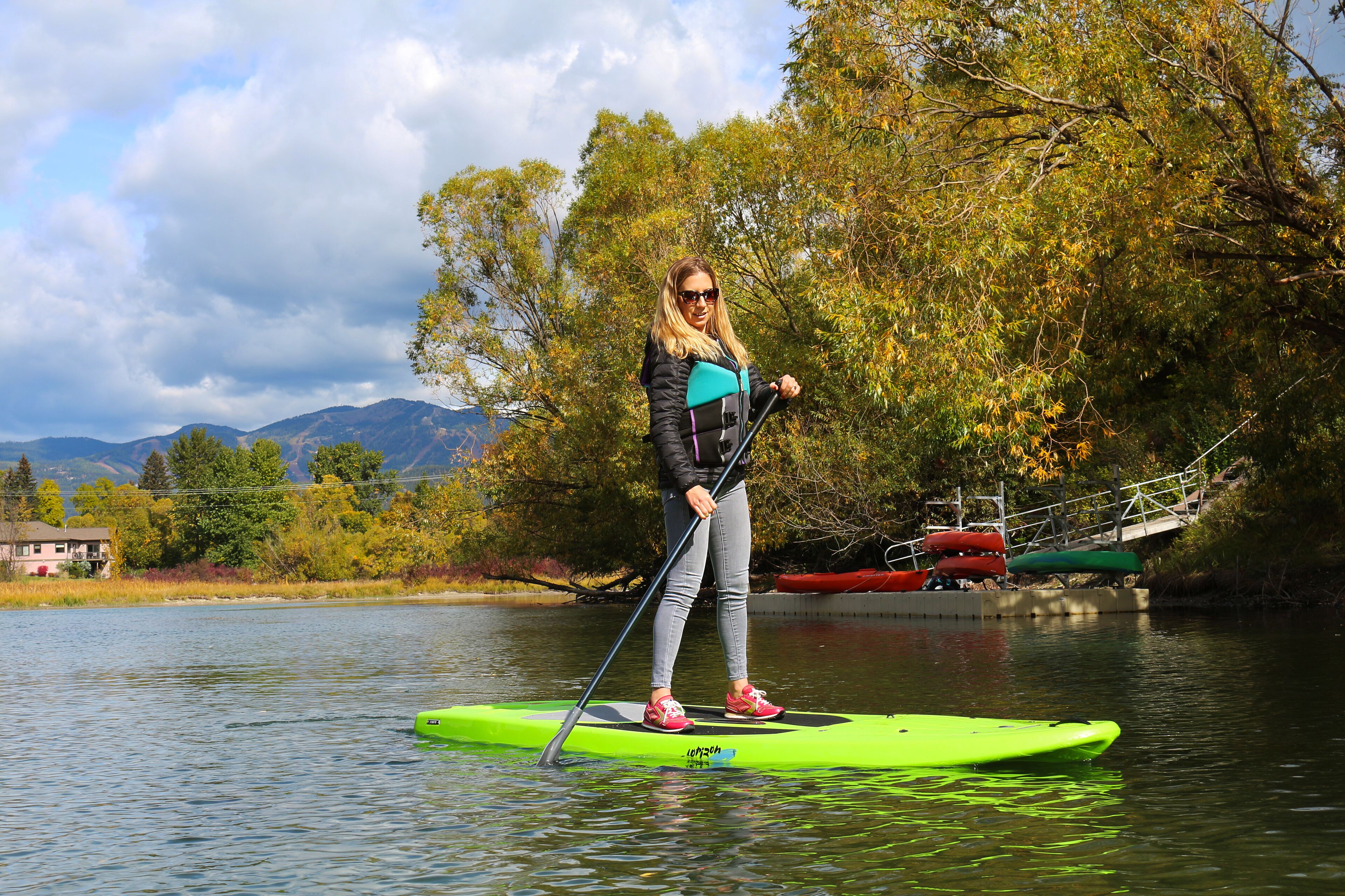 A person standing on a paddleboard in a body of water with boats and trees in the background.